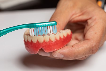 Patient using toothbrush to clean denture