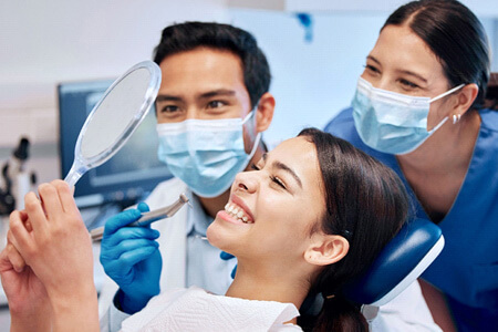 patient smiling at reflection with dentist and dental assistant