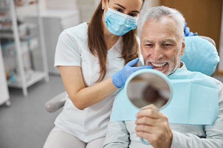 An older man admiring his new dental implants in a hand mirror