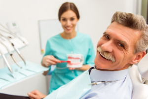 Dentist smiles in background while denture patient in foreground smiles