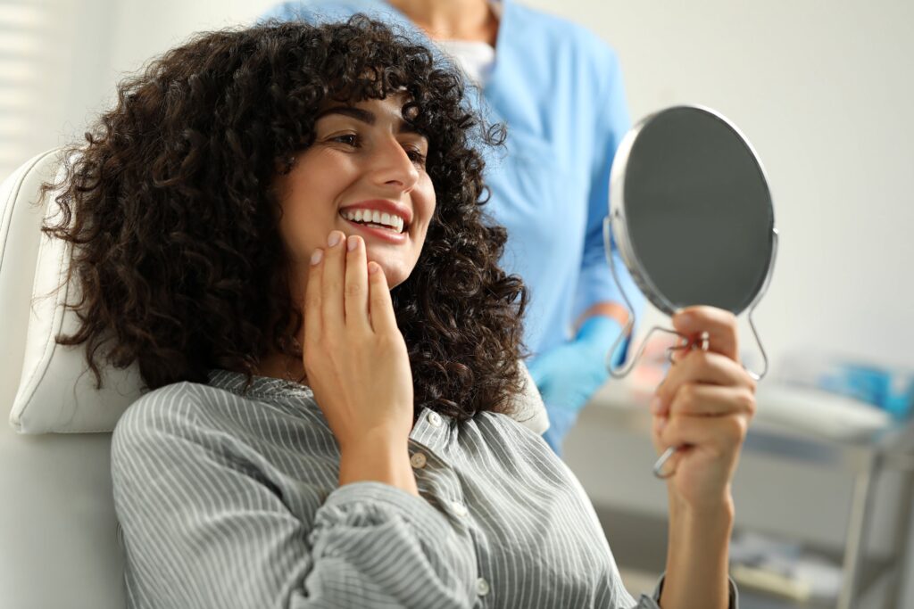 Woman with curly hair in dental chair admiring reflection in mirror